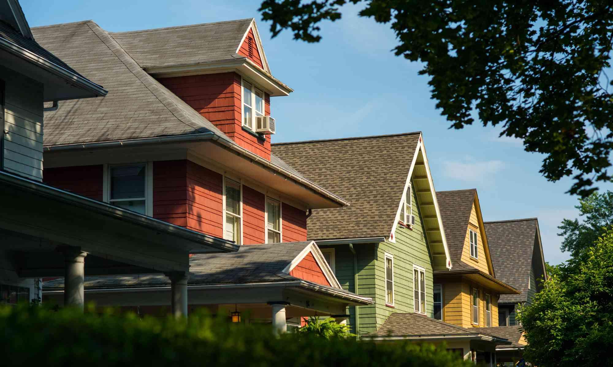 The upper halves of about five Rochester, New York, houses framed by green trees and shrubs and a blue sky to illustrate the University of Rochester's expanded home ownership incentive program.